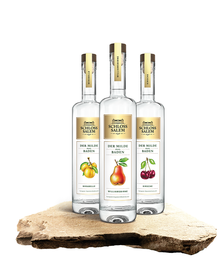 Produktbild von drei Flaschen Obstspirituose - Williamsbirne, Mirabelle und Kirsche - die auf einem Stein stehen. Die Marke heißt Schloss Salem, die Submarke ist Der Milde aus Baden.
